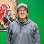 A Little Guys Mover in grey sweatshirt in front of a green wall and striking painting.