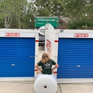 A Little Guys mover sits on a roll of bubble wrap in front of two PODS containers