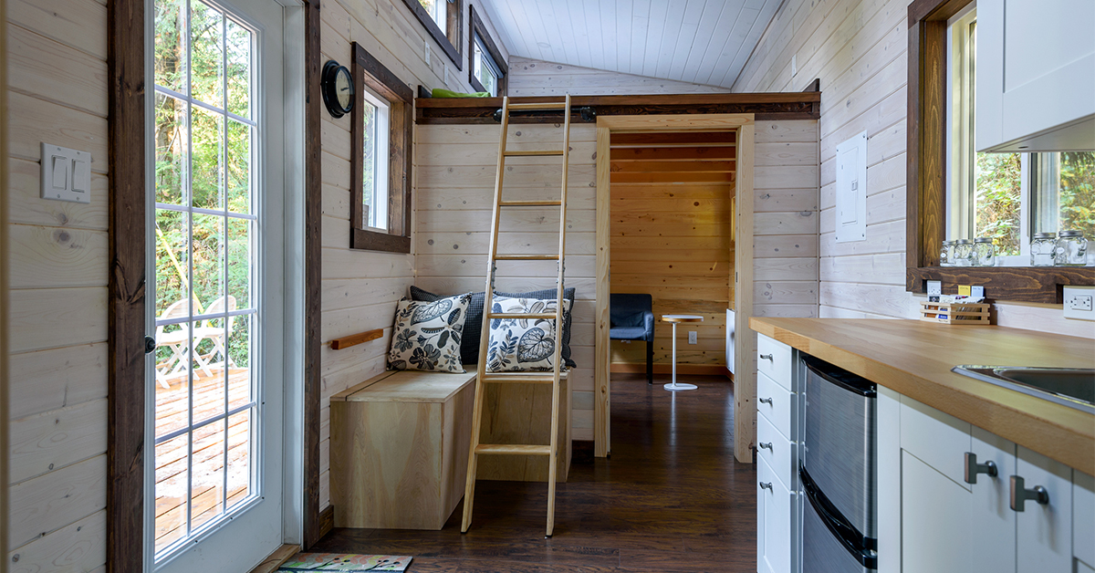 A view of a tiny house furnished with a ladder, a built-in bench, and a chair with a side table.