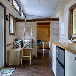 A view of a tiny house furnished with a ladder, a built-in bench, and a chair with a side table.