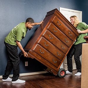 Two Little Guys movers move a chest of drawers out of a room.