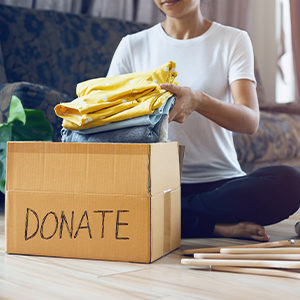 A person packs clothes inside a cardboard box for donation.