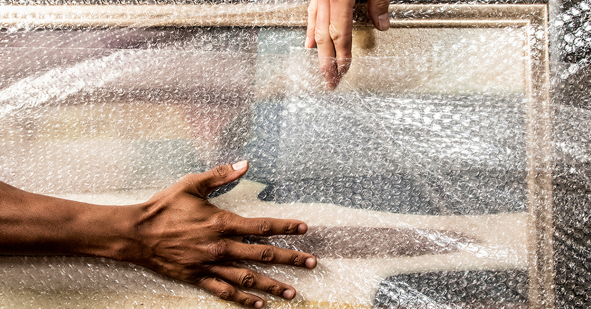 Hands from two Little Guys wrap a framed artwork in bubble wrap.