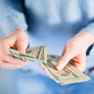 A person counting 20 dollar bills to hand to someone.