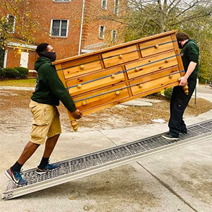 Two Little Guys movers carefully walk a heavy dresser up the moving truck ramp.