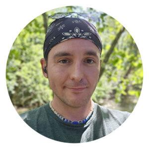 Little Guys mover Neil with a green shirt and bandana covering his head. He's outside surrounded by peaceful green trees and sunshine.