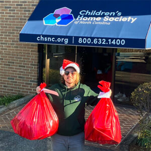 A Little Guys Movers mover in a Santa hat holds up two large red bags full of donated toys.