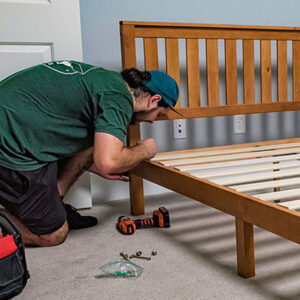 A mover with Little Guys Movers disassembles a bed for a contractor.