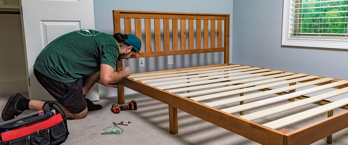 A mover with Little Guys Movers disassembles a bed for a contractor.