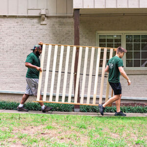 Two Little Guys Movers movers move a bed frame across an apartment complex in Raleigh.