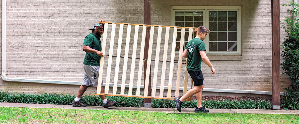 Two Little Guys Movers movers move a bed frame across an apartment complex in Raleigh.