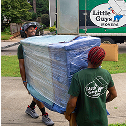 Two Little Guys Movers carefully move an awkwardly shaped item to a moving truck.