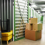 A pile of filled cardboard boxes outside a storage unit that already contains furniture.