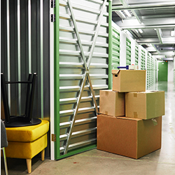 A pile of filled cardboard boxes outside a storage unit that already contains furniture.