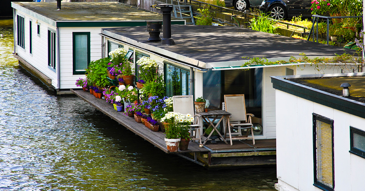 A house boat on the water with beautiful plants on the front porch