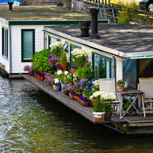 A house boat on the water with beautiful plants on the front porch