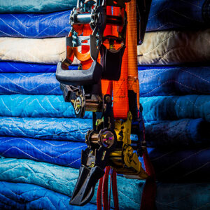 A stack of blue moving blankets behind several orange and black ratchet straps