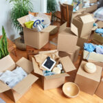 Several moving boxes are stacked in an apartment. Some boxes are open as if in the process of being packed.
