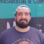 Smiling mover wearing a backwards hat, standing in front of moving truck