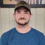 Mover in blue t-shirt and tan ball cap smiles at the camera