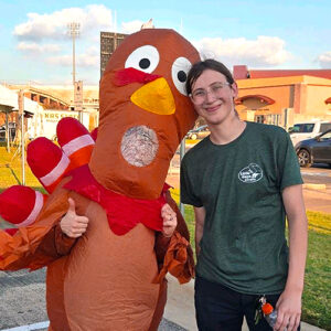 A person in a Little Guys Movers t-shirt poses with someone dressed up like a turkey